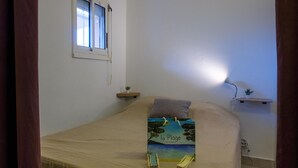 Ein Schlafzimmer mit Bett, Fenster, Nachttisch und einer Wandregal mit Pflanze.