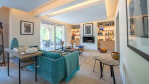 A modern living room with a teal sofa, a coffee table, and a dining area with a small table and chairs. There is a fireplace and a kitchen area visible in the background. - Villa with pool 2.5km from Saint-Tropez (Gassin)