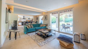 A spacious living area with a teal sofa, a coffee table, and a view of the kitchen and outdoor patio. - Villa with pool 2.5km from Saint-Tropez (Gassin)