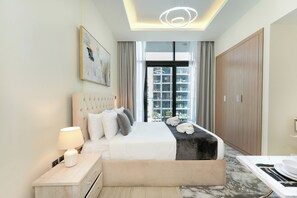 A modern hotel room with a large bed, a bedside table with a lamp, a view of the city through large windows, and a wooden wardrobe. - PVH - Azizi Riviera - Posh Studio  (Dubai)