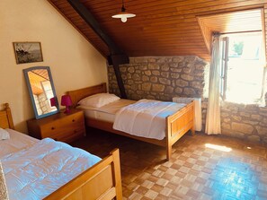 Ein Zimmer mit zwei Holzbetten, einer Steinwand, einer Holzbalkendecke und einem Fenster mit Vorhängen.