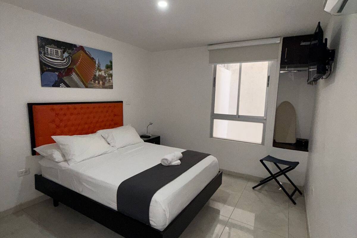 A modern bedroom with a bed, a small table, a window, and a wall-mounted TV.