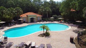 Piscina com espreguiçadeiras e guarda-sóis, cercada por árvores e um edifício com telhado em azulejos.