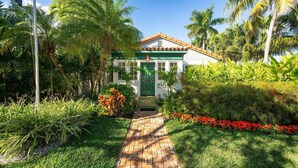 A house with a green door, surrounded by lush greenery and a brick pathway leading to the entrance. - Monthly rental-1 level, 4-bed, 3 bath, quiet home, private sunny pool, parking (Key West)