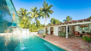 A swimming pool with a tiled edge, surrounded by palm trees and a covered patio area with outdoor furniture. - Monthly rental-1 level, 4-bed, 3 bath, quiet home, private sunny pool, parking (Key West)