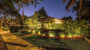 A well-lit building with a red roof, surrounded by lush greenery and a pathway leading to it. - Monthly rental-1 level, 4-bed, 3 bath, quiet home, private sunny pool, parking (Key West)