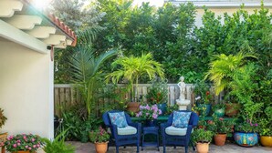 A patio with two wicker chairs, a small table, and various potted plants. - Monthly rental-1 level, 4-bed, 3 bath, quiet home, private sunny pool, parking (Key West)