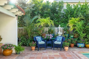A patio with two wicker chairs, a small table, and various potted plants. - Monthly rental-1 level, 4-bed, 3 bath, quiet home, private sunny pool, parking (Key West)