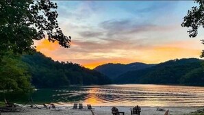 A lakeside setting with chairs and tables arranged on the sand, overlooking the water. - Best of Bear Lake | Pool • Golf • Lake & Mtn Views (Tuckasegee)