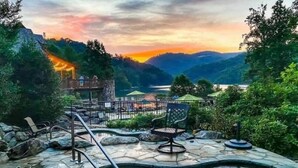 A hot tub area with a stone deck, lounge chairs, and a view of a lake and mountains during sunset. - Best of Bear Lake | Pool • Golf • Lake & Mtn Views (Tuckasegee)