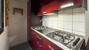 A compact kitchen with a gas stove, stainless steel sink, and red cabinets. - Residenze Cielo e Mare - Conchiglia (San Teodoro)