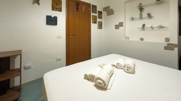 A hotel room with a bed, a wooden wardrobe, a shelf with decorative items, and a wall-mounted thermostat. - Residenze Cielo e Mare - Conchiglia (San Teodoro)