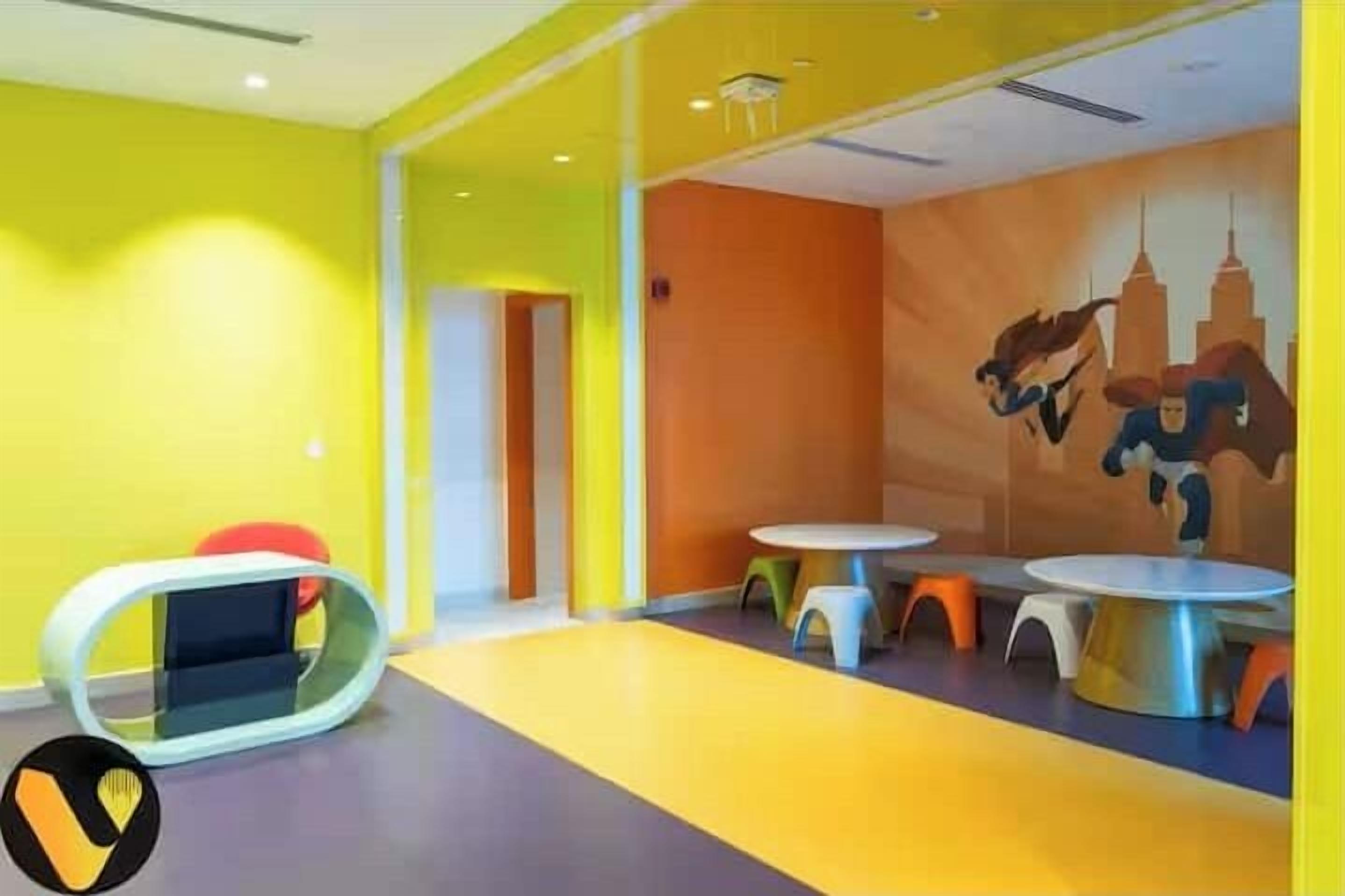 A brightly colored children's play area with yellow walls, orange accents, and a mural of superheroes.
