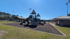Un parque infantil con toboganes y estructuras para escalar, rodeado de césped y un edificio.