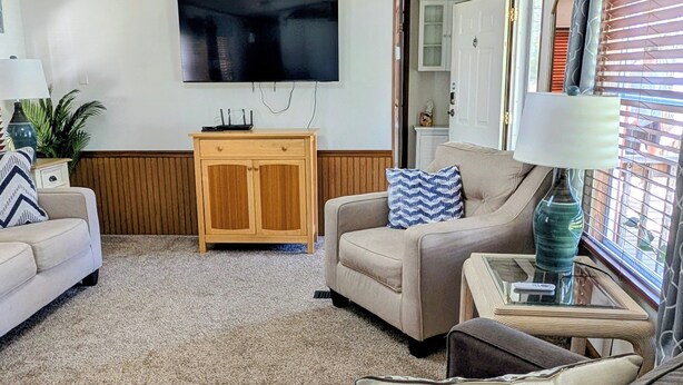 Una sala de estar con una televisión de pantalla plana, dos sofás, un mueble de madera y una mesa de centro de vidrio.