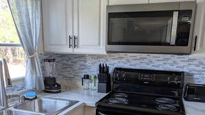 Una cocina con armarios blancos, una estufa negra, un microondas y un lavabo.