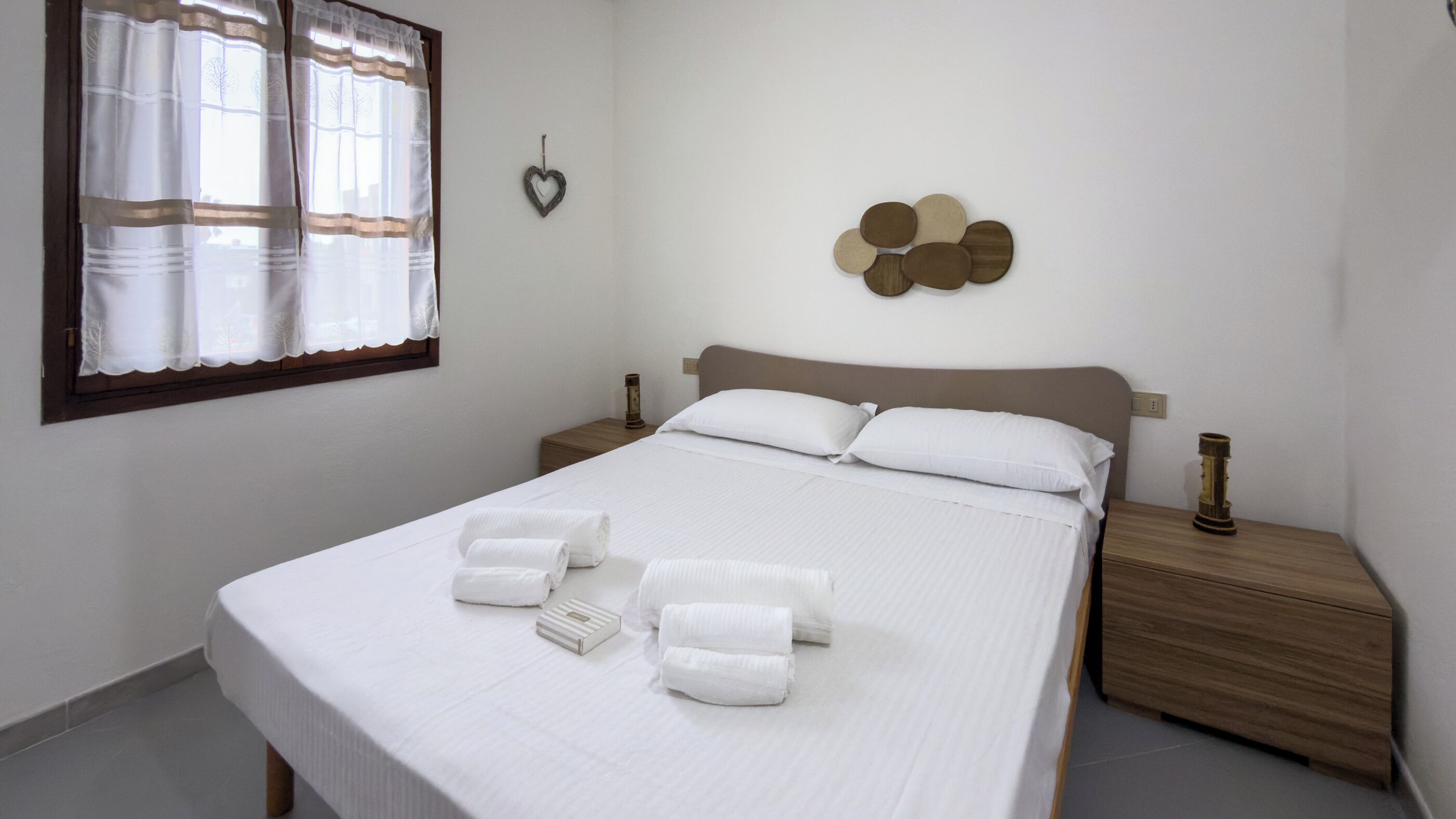 Ein ordentlich gemachtes Bett mit weißen Leinen und Handtüchern, ein hölzernes Kopfteil und ein Nachttisch mit Lampe.