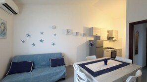 Un espacio habitable compacto con un sofá azul, una mesa de comedor y una kitchenette.