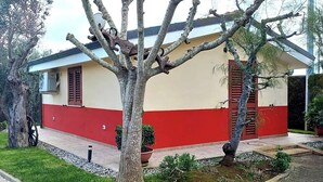 Un bâtiment à la façade rouge et beige, avec un arbre au premier plan et un petit jardin.