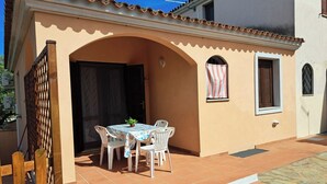 A patio with a table and chairs, a small garden, and a building with a tiled roof and arched doorway. - Residenze Cielo e Mare - Sole (San Teodoro)