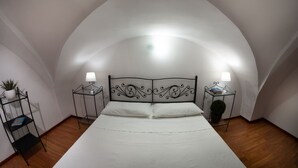 Ein Schlafzimmer mit gewölbter Decke, einem Bett mit weißer Bettwäsche, zwei Nachttischen mit Lampen und einem kleinen Regal mit einer Pflanze.