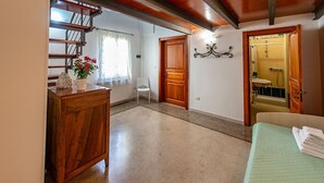 Ein Zimmer mit Holzboden, einem Bett, einem kleinen Tisch mit einer Vase, einem Stuhl und einer Treppe, die in ein weiteres Zimmer führt.