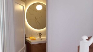 Un bagno con un lavabo in marmo, uno specchio rotondo e una porta bianca.