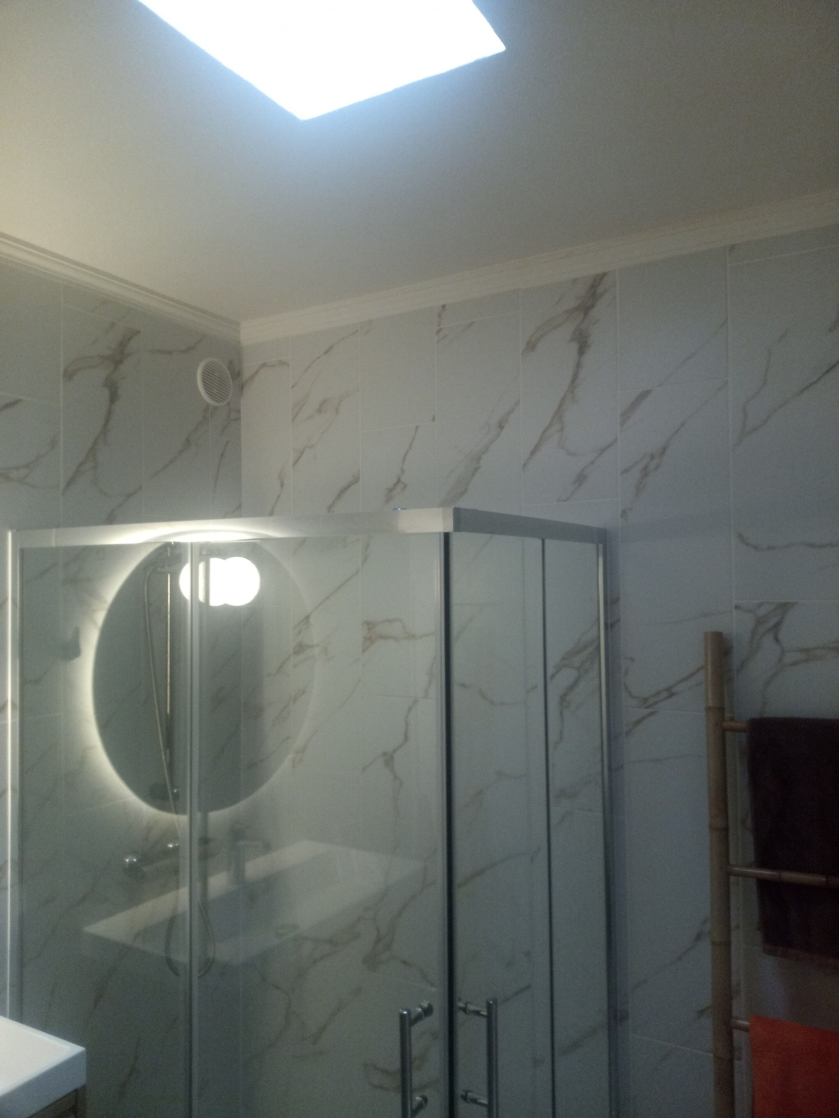 Une salle de bain avec une douche à parois de verre, des murs en marbre et un porte-serviettes.