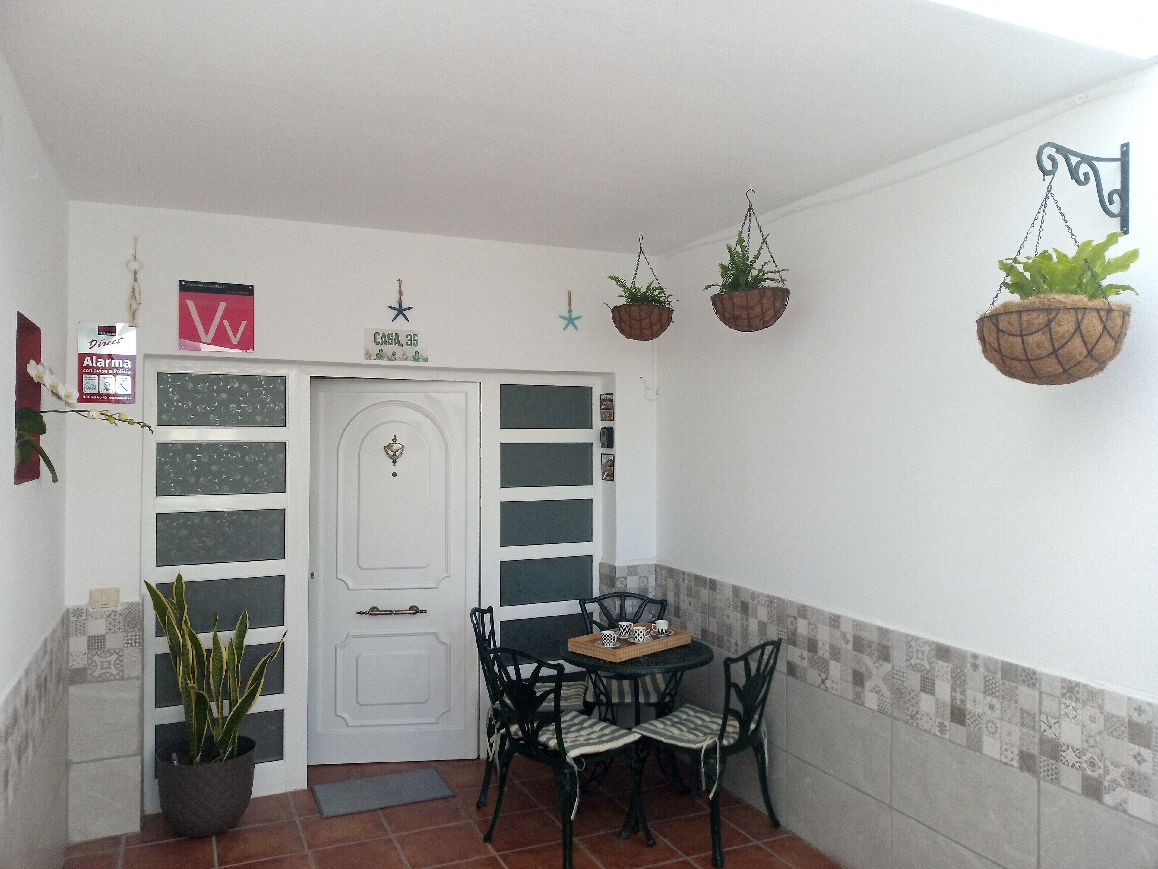 A small dining area with a white door, a table with chairs, and hanging planters.
