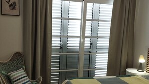 Una camera da letto con un letto, una sedia, un comodino e una finestra con tende.