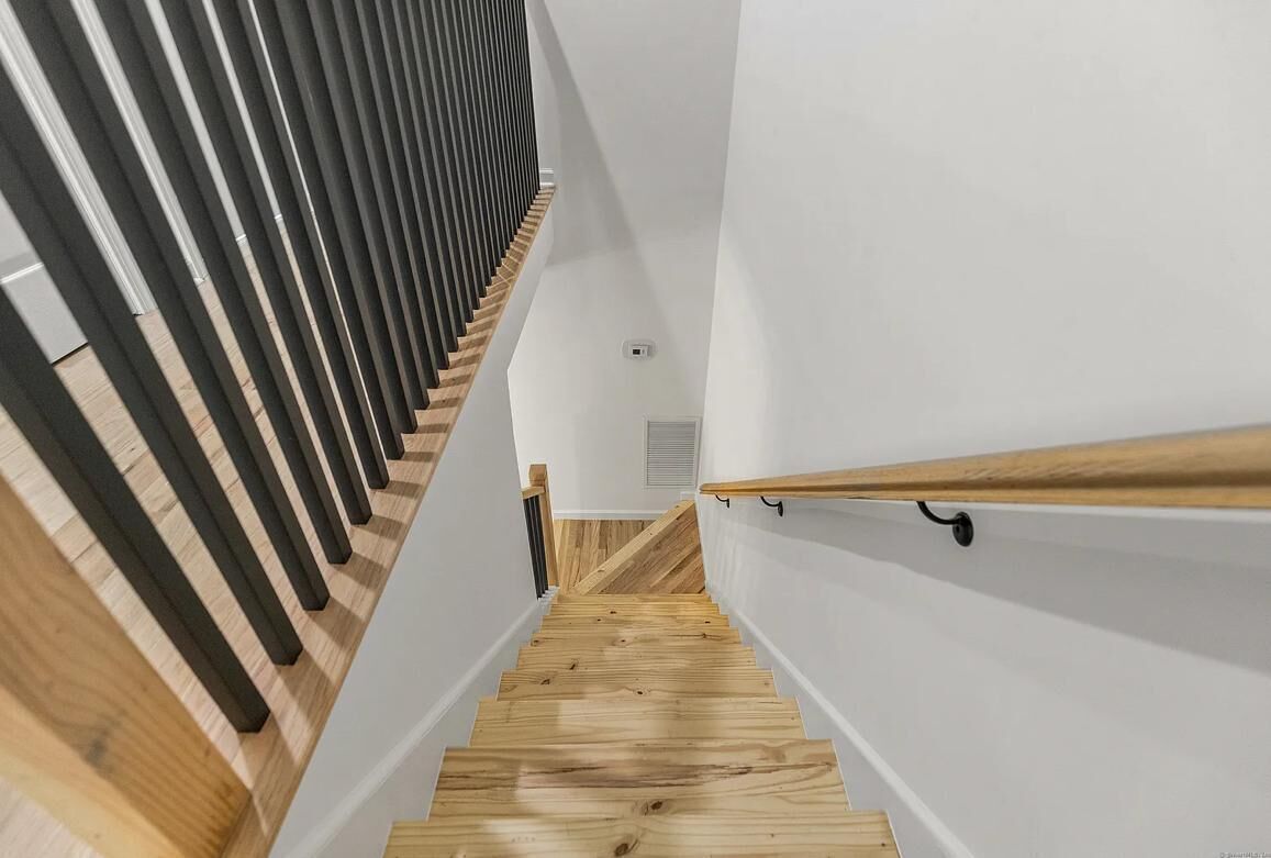 A wooden staircase with a modern design, white walls, and a wooden handrail.