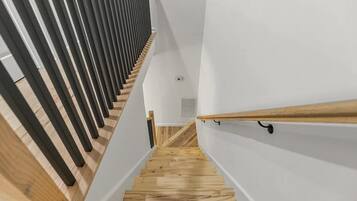 A wooden staircase with a modern design, white walls, and a wooden handrail.