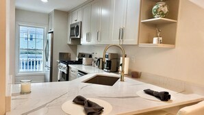 Una cocina moderna con armarios blancos, un refrigerador de acero inoxidable, un microondas y una estufa a gas.