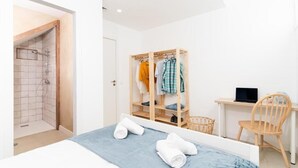 A bedroom with a bed, a wooden wardrobe, a desk with a laptop, a chair, and a shower area. - Bucio Coliving (Arona)