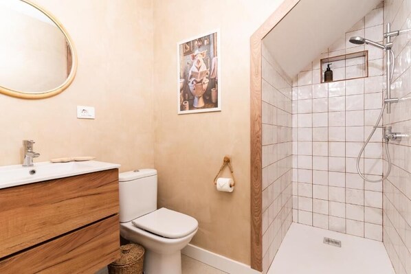 A bathroom with a wooden vanity, a toilet, a shower with a glass enclosure, and a framed picture on the wall. - Bucio Coliving (Arona)