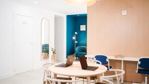 A modern meeting room with a round table, chairs, laptops, a hanging light fixture, and a blue accent wall. - Bucio Coliving (Arona)