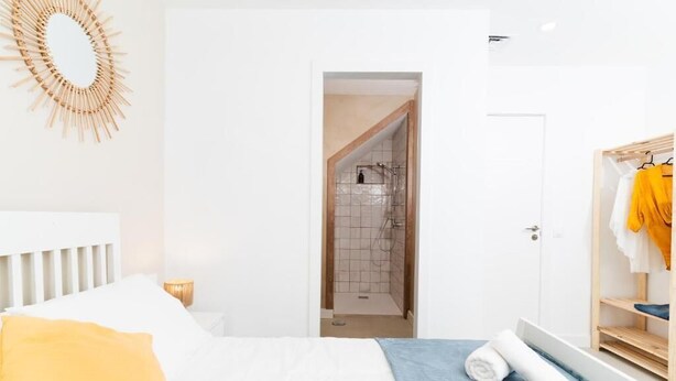 A bedroom with a bed, a wooden wardrobe, a bathroom with a shower, and a hallway. - Bucio Coliving (Arona)