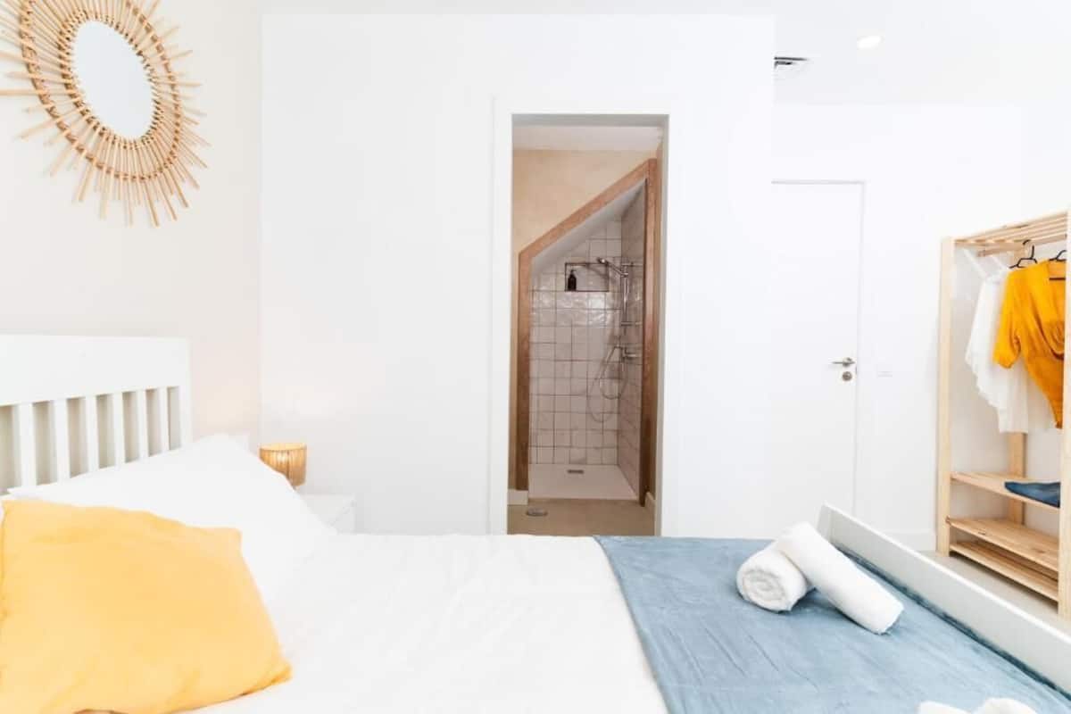 A bedroom with a bed, a wooden wardrobe, a bathroom with a shower, and a hallway.
