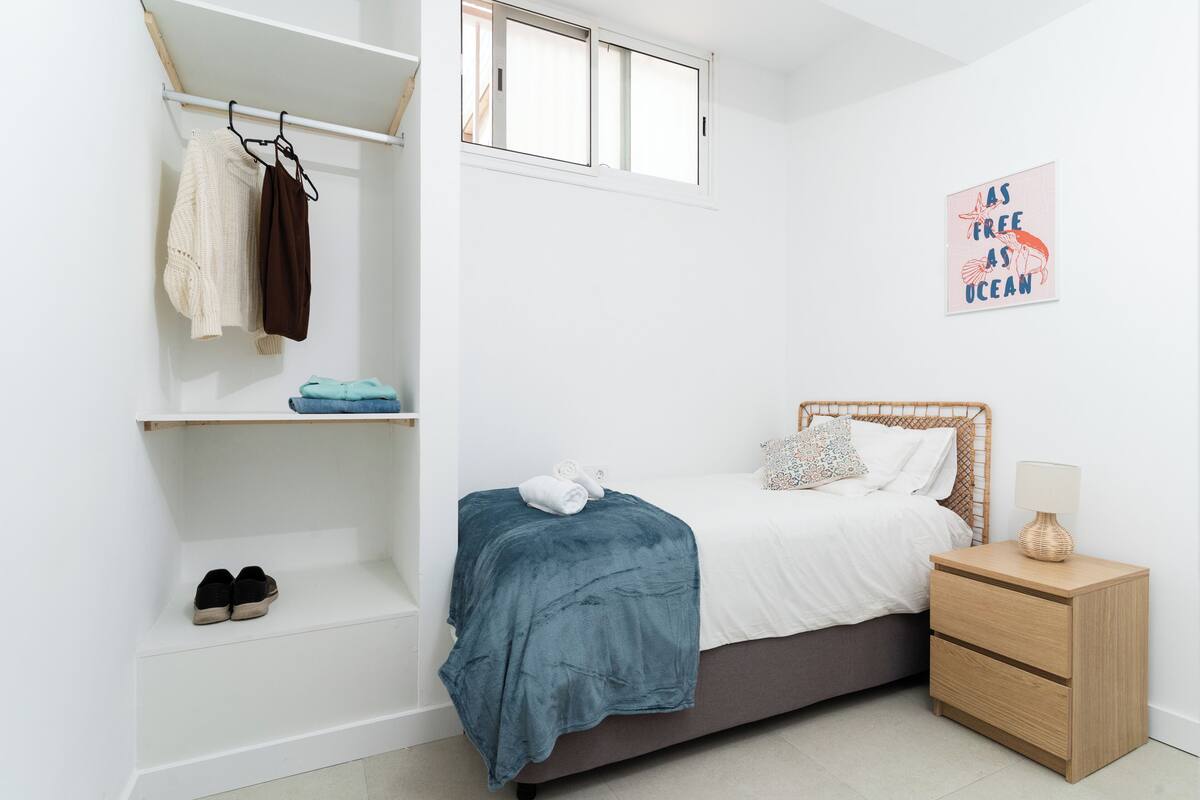 A bedroom with a bed, a nightstand, a shelf with shoes, a window, and a wall art piece.