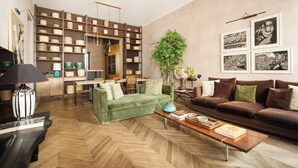 Una sala de estar moderna con piso de espiga, sofás verde y marrón, una mesa de centro con libros y una estantería llena de objetos decorativos.