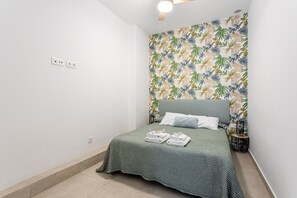Ein Schlafzimmer mit einem Bett, einer Wand mit Blattmuster, einem Deckenventilator und einem Nachttisch mit Lampe.