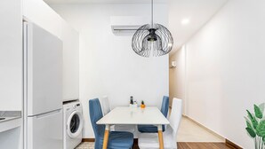 A compact kitchen with a washing machine, a dining table with chairs, and a pendant light. - Holiday Home 'Portal A Valencia' with Wi-Fi and Air Conditioning (València)