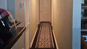 En smal hall med en mönstrad matta, en vit dörr längst ner och en taklampa.