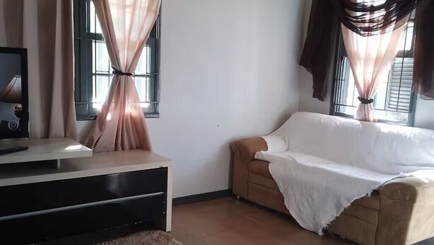 Una sala de estar con un sofá, un televisor sobre un mueble bajo y cortinas en las ventanas.