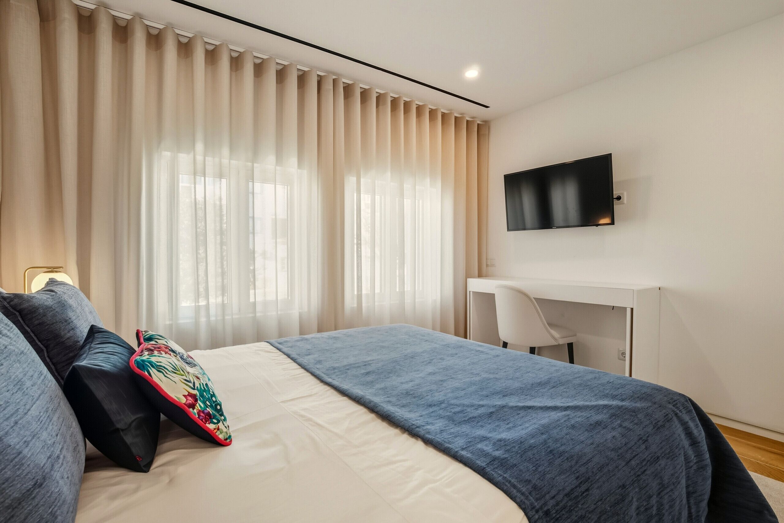 Une chambre d’hôtel moderne, dotée d’un grand lit, d’un bureau et d’un téléviseur fixé au mur.