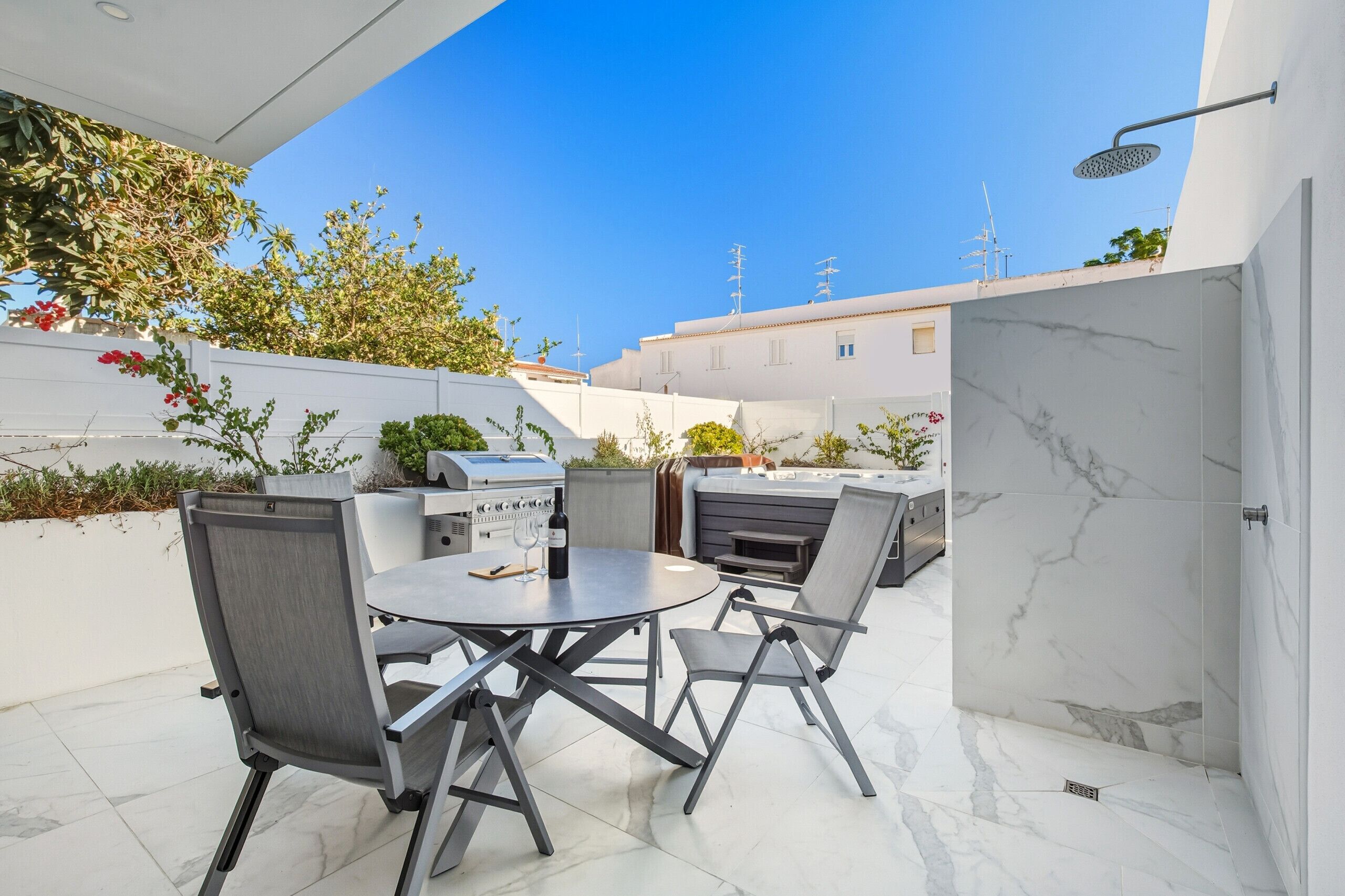 An outdoor patio with a round table, chairs, a grill, and a shower.