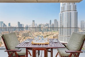 Ein Balkon mit zwei Stühlen und einem Tisch, gedeckt für das Frühstück, mit Blick auf eine Skyline mit Hochhäusern.