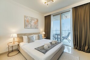 Ein modernes Hotelzimmer mit einem großen Bett, zwei Nachttischen mit Lampen, Blick auf die Stadt durch raumhohe Fenster und einem Balkon mit Sitzgelegenheit.