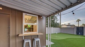 A covered patio area with a window overlooking a well-maintained lawn and a golf course. - Scottsdale Oasis | Pool, Firepit, Putting Green (Scottsdale)