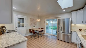 A modern kitchen with a dining area, a large refrigerator, and a sliding glass door leading to a patio. - Scottsdale Oasis | Pool, Firepit, Putting Green (Scottsdale)